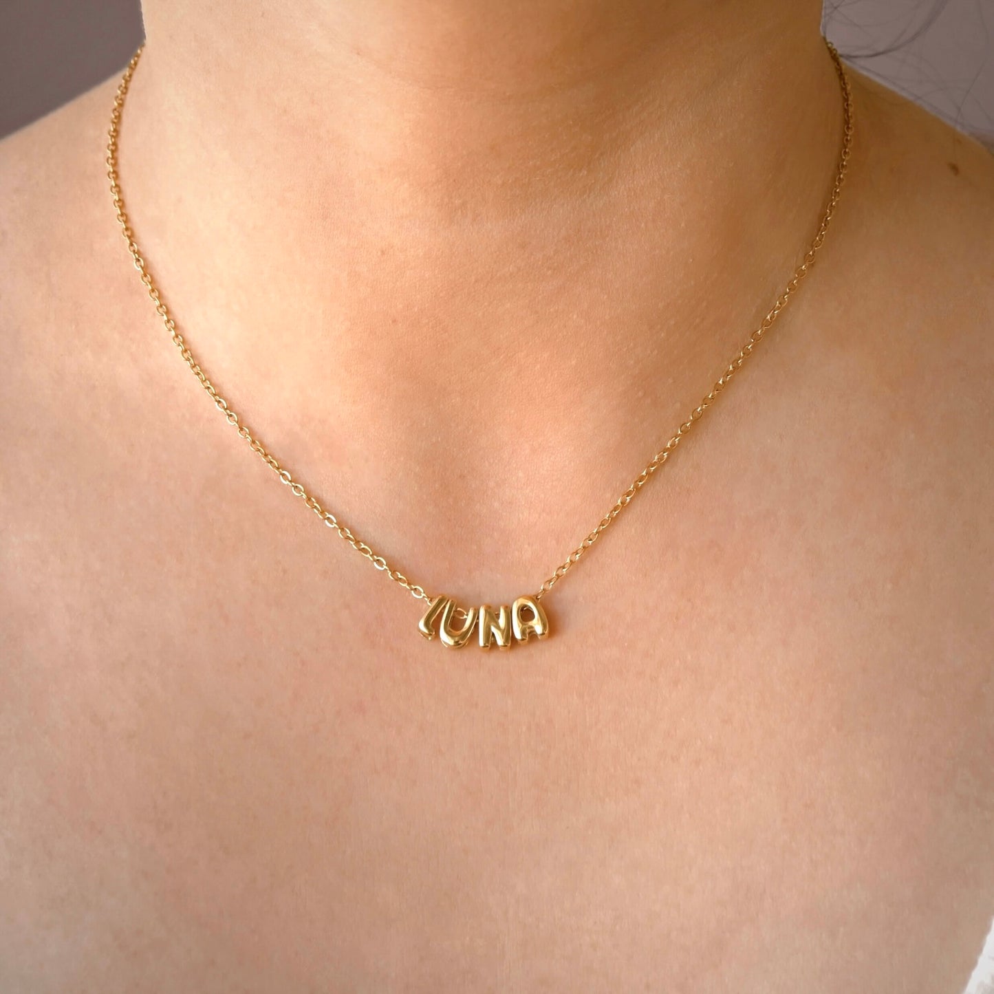 A gold chain necklace with a personalized nameplate spelling 'LUNA' worn on a person's neck.