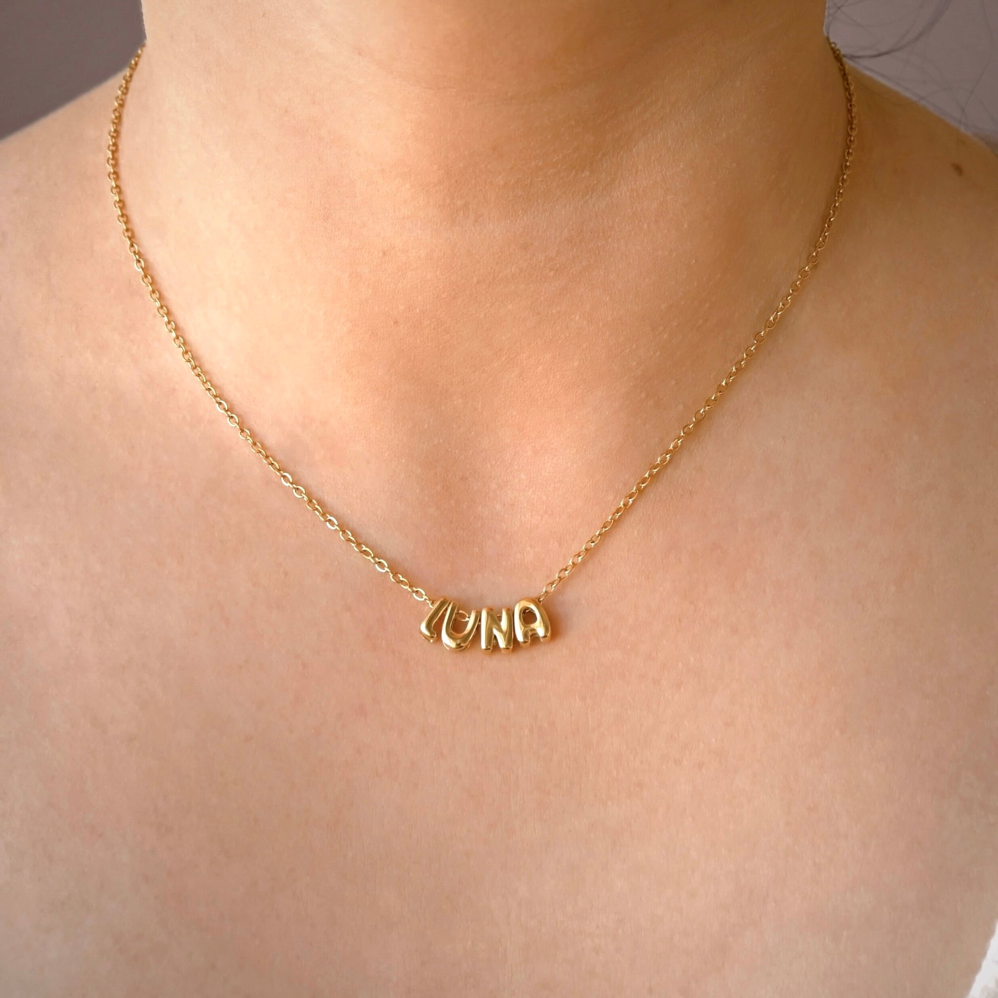 A gold chain necklace with a personalized nameplate spelling 'LUNA' worn on a person's neck.