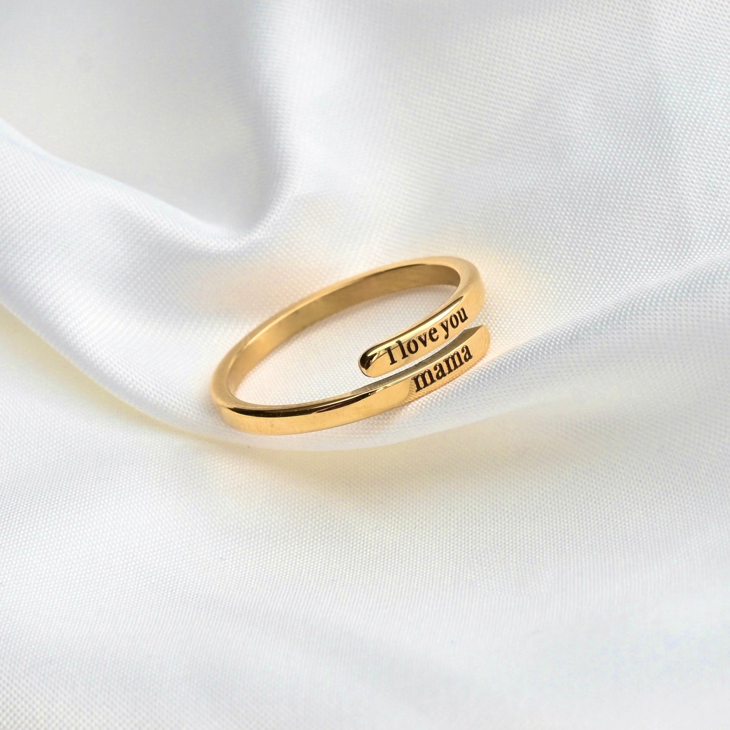 Gold ring with 'I love you mama' engraving on a white fabric background