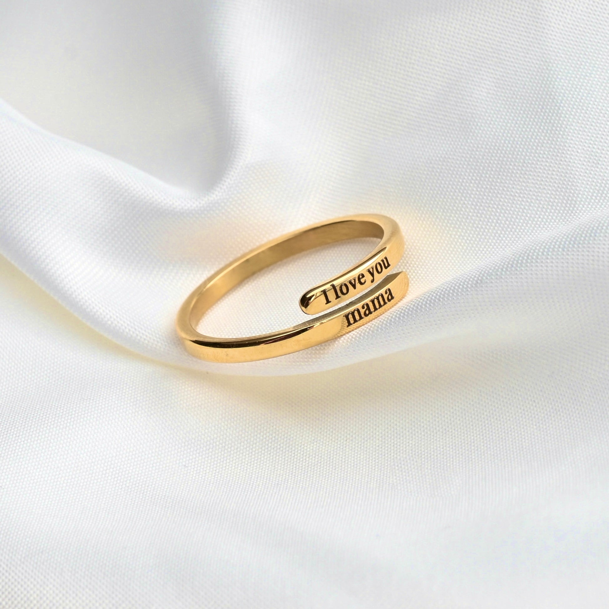 Gold ring with 'I love you mama' engraving on a white fabric background