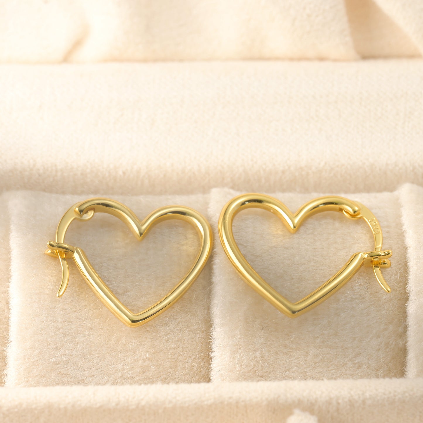 Gold heart-shaped hoop earrings with S925 stamp on latch back clasp on a soft beige background