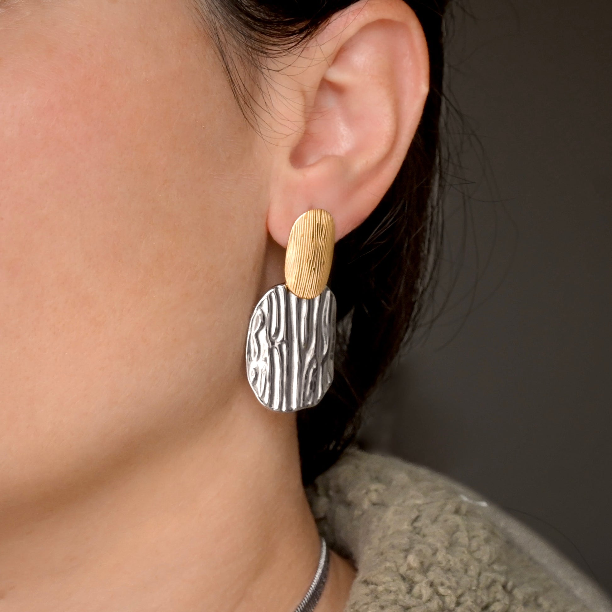 Close-up of a person wearing large textured two tone dangle earrings 