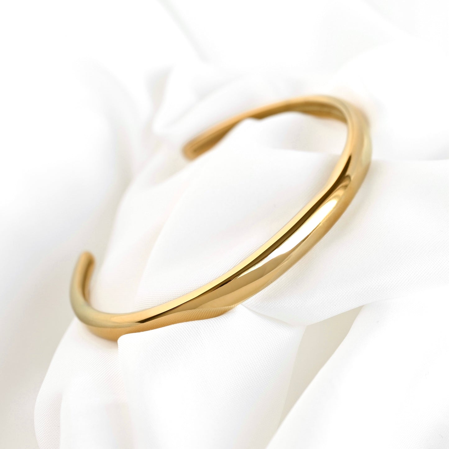 Gold cuff bracelet on a white fabric background