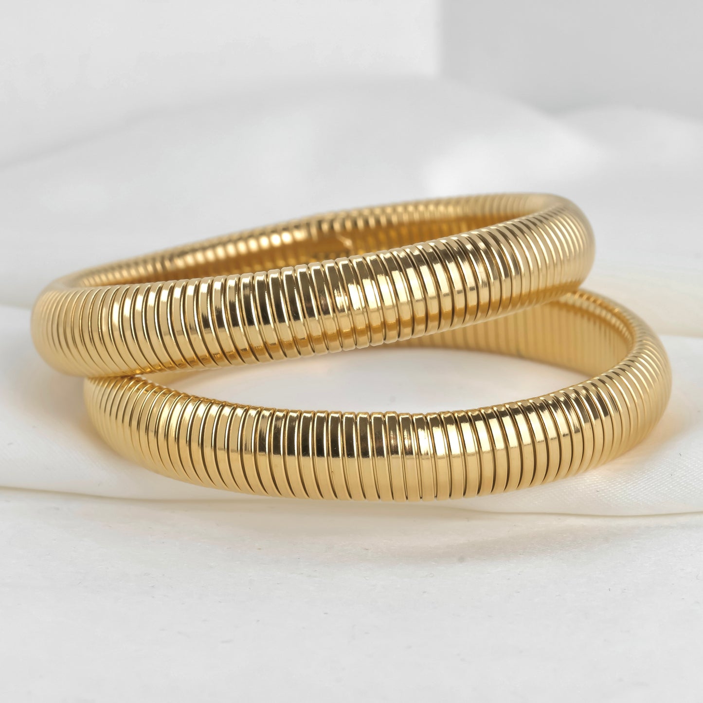 Two gold expandable bangles on a white background