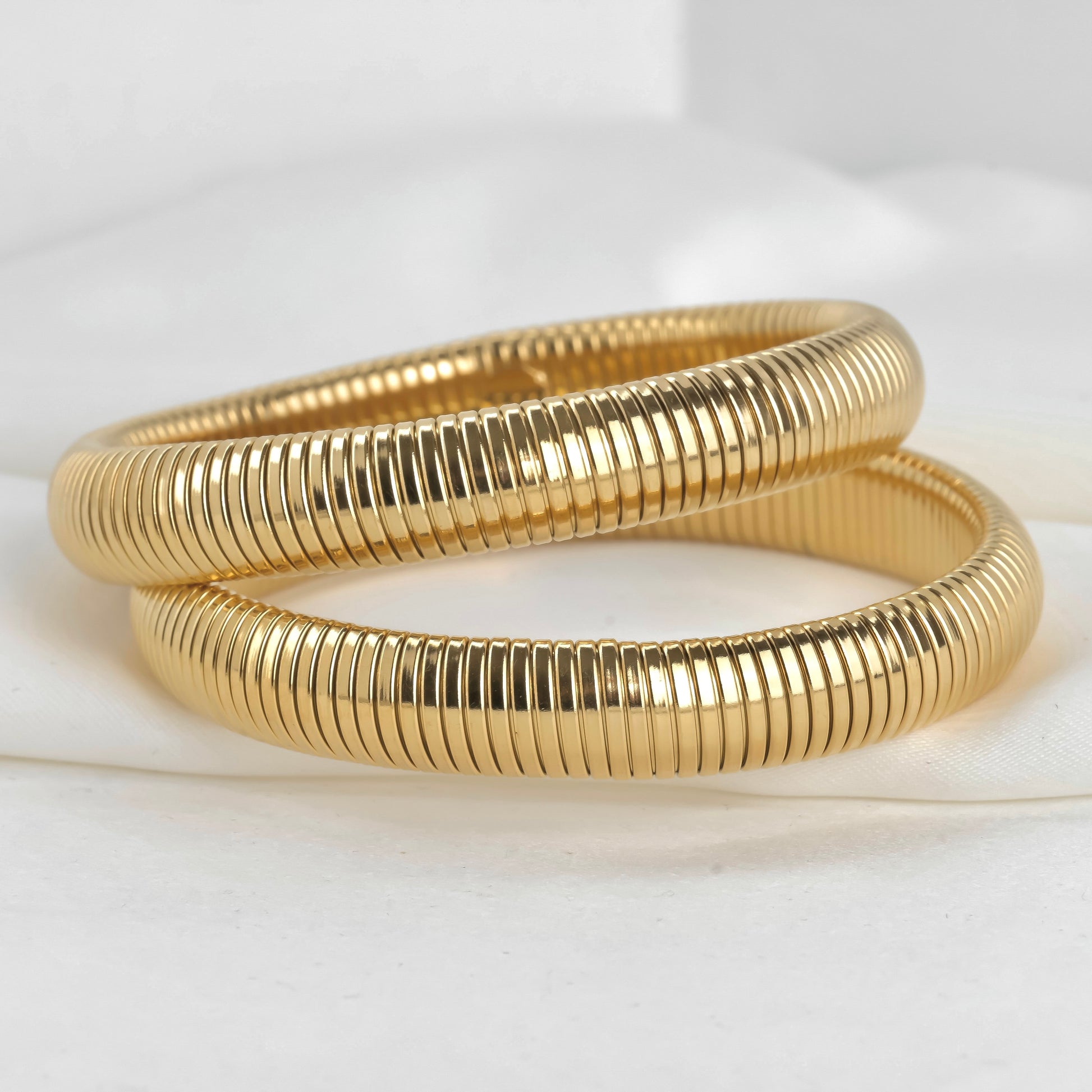 Two gold expandable bangles on a white background