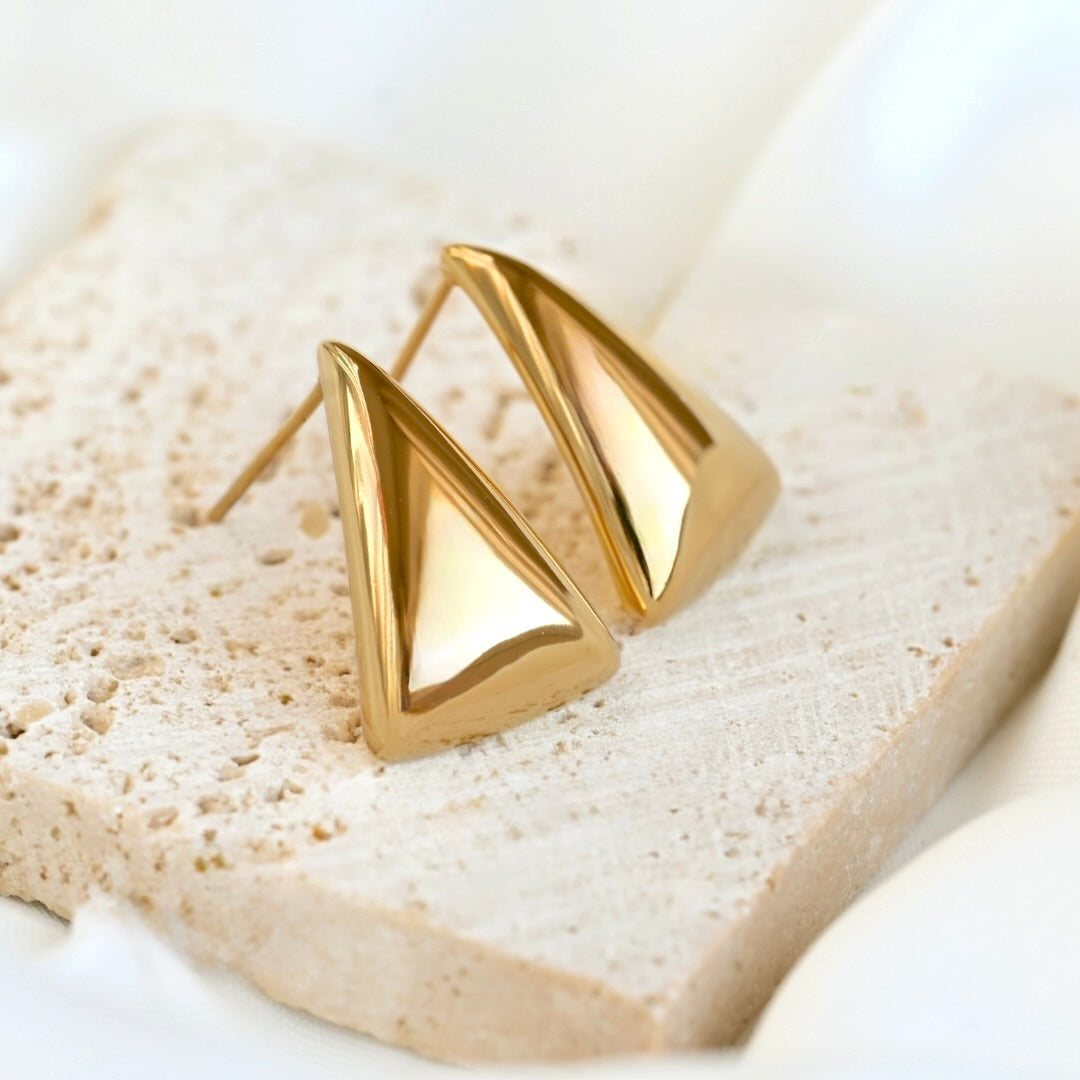 18k Gold medium triangle stud earrings on a textured stone surface