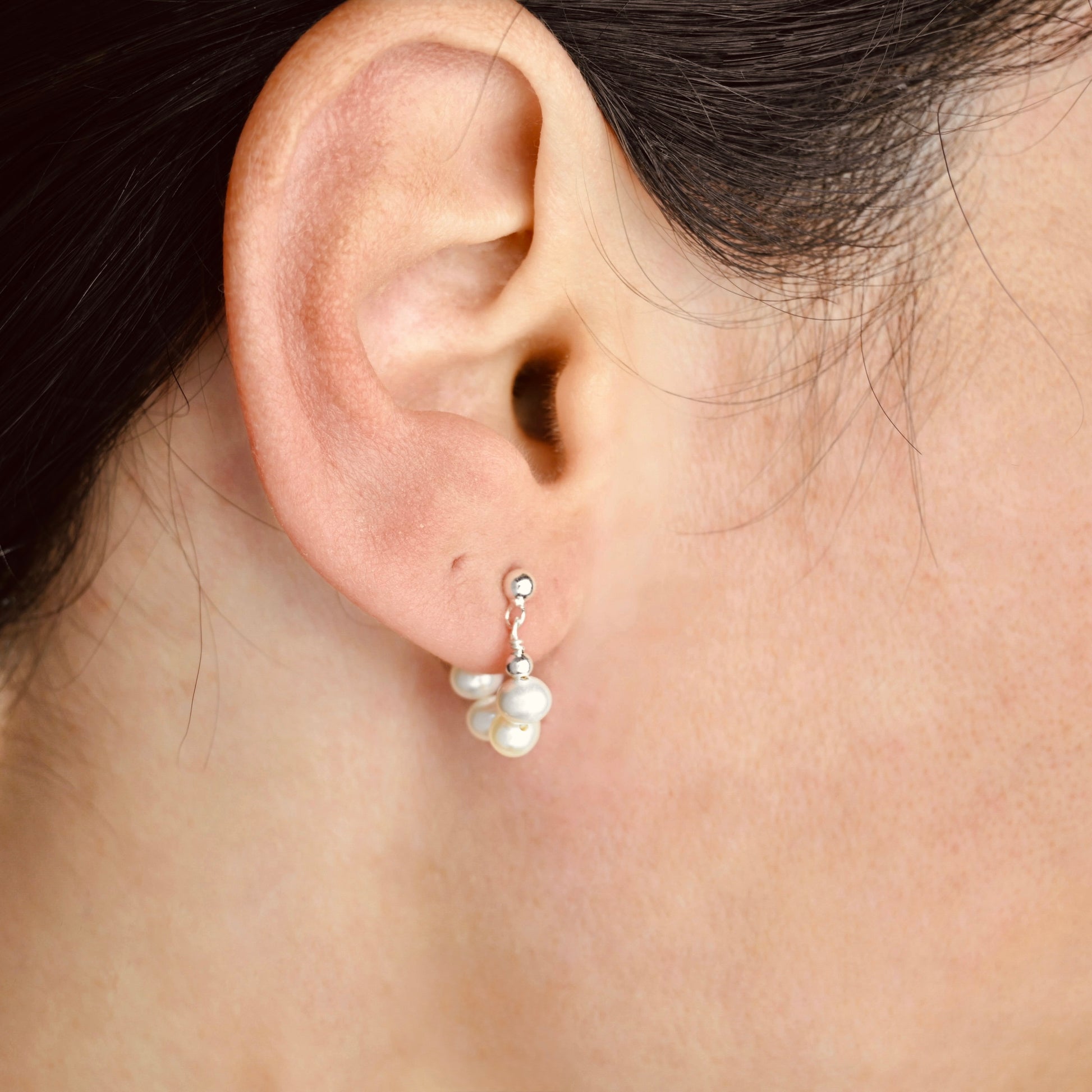 Close-up of an ear wearing silver pearl earrings with a blurred background