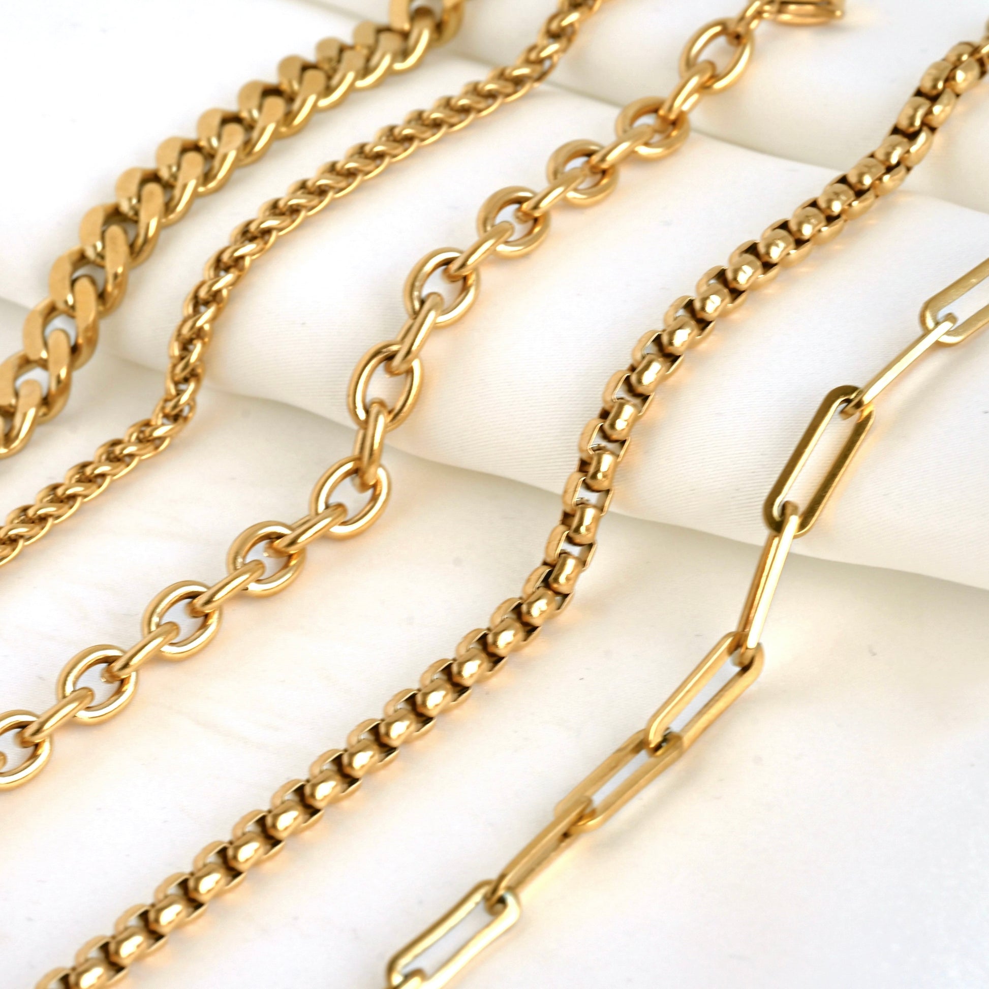 Thick gold chains of different designs including paperclip, rounded box, rolo, wheat and cuban links on a white background