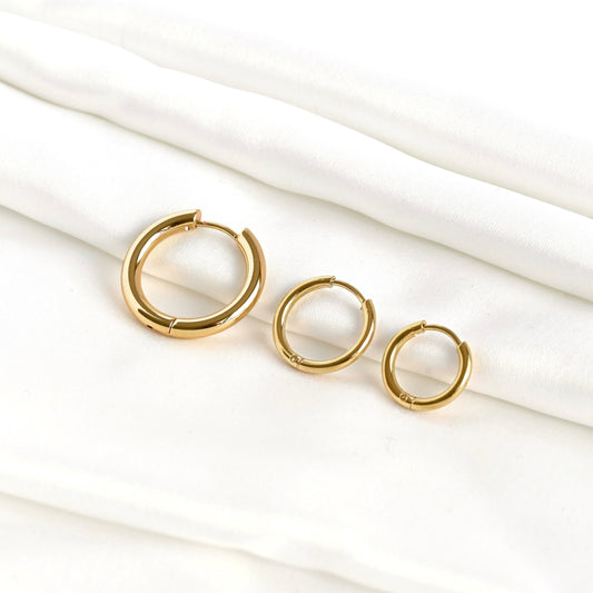 Three simple gold hoop earrings in graduated sizes on a white fabric background