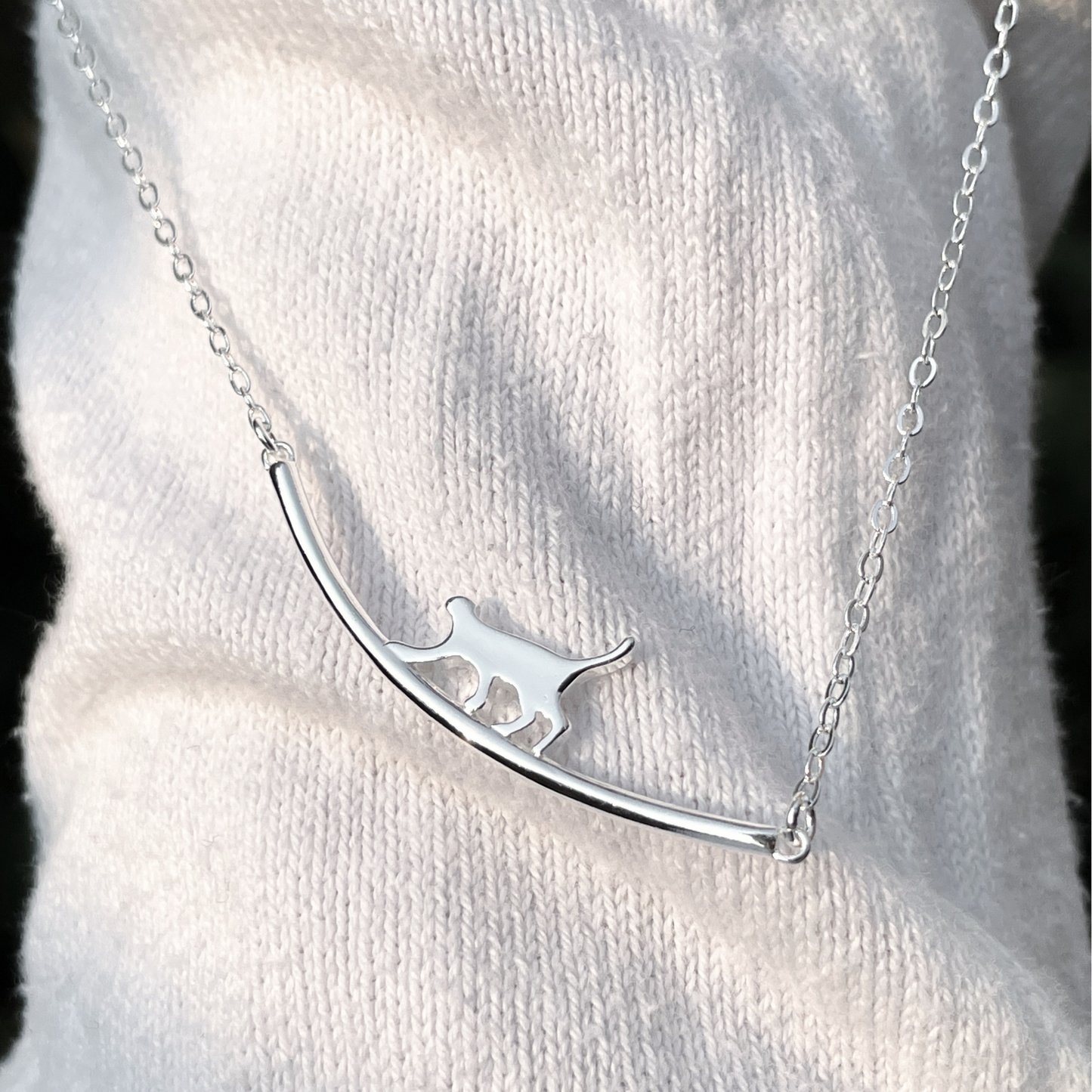 Silver cat necklace with a curved bar design on a white sweater under direct sunlight