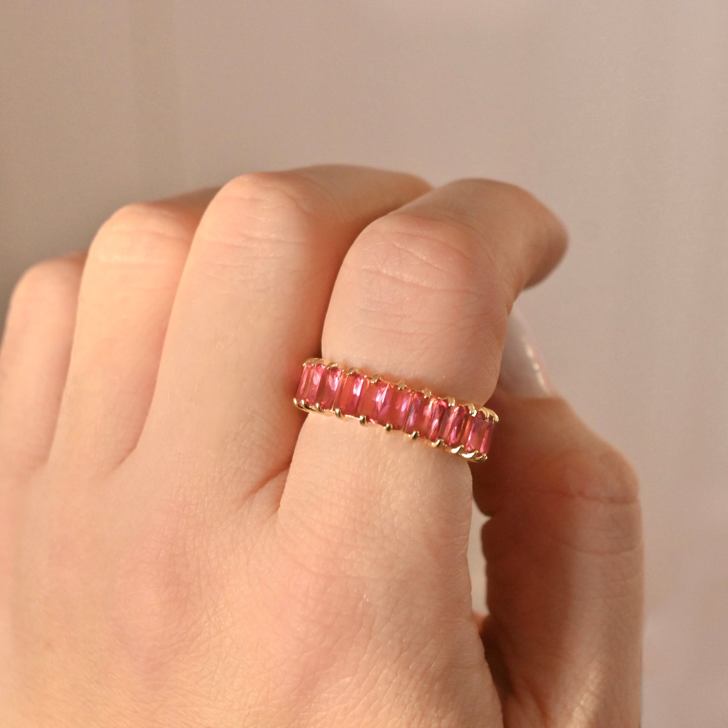 Gold ring with july birthstone on a hand against a neutral background