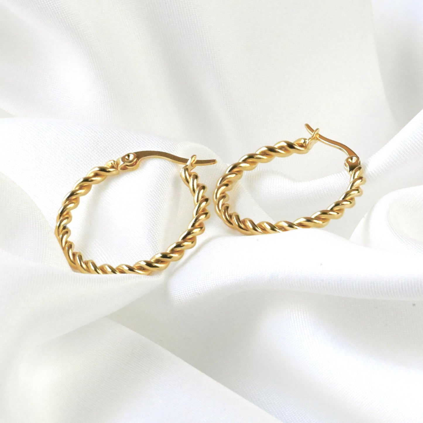 Gold rope hoop earrings on a white fabric background