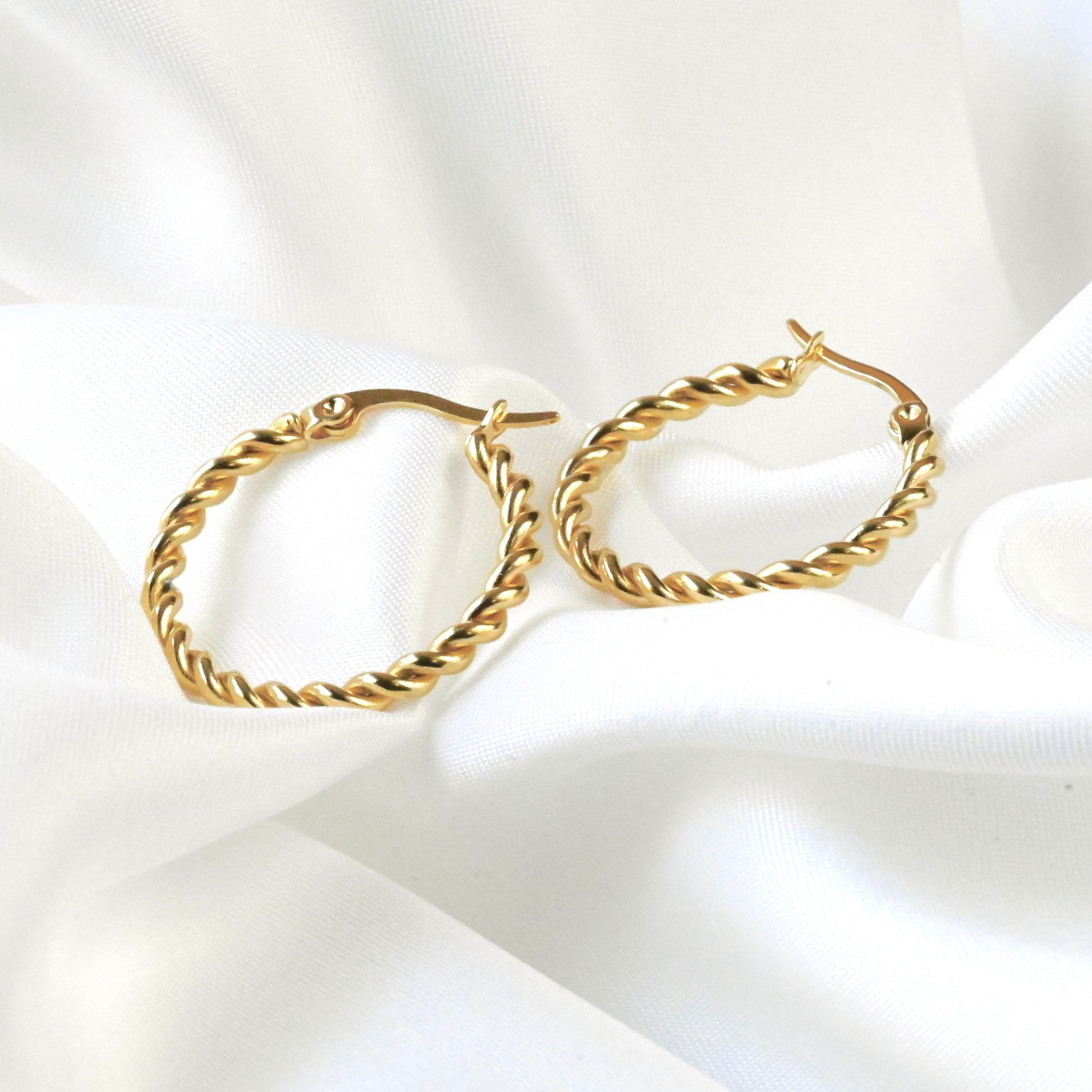 Gold rope hoop earrings on a white fabric background
