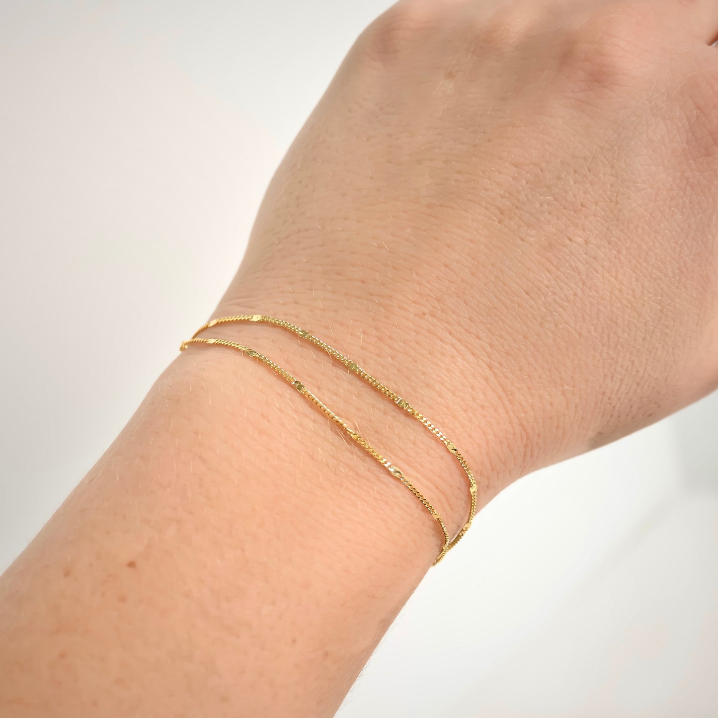 Gold two layered bracelet on a wrist against a white background