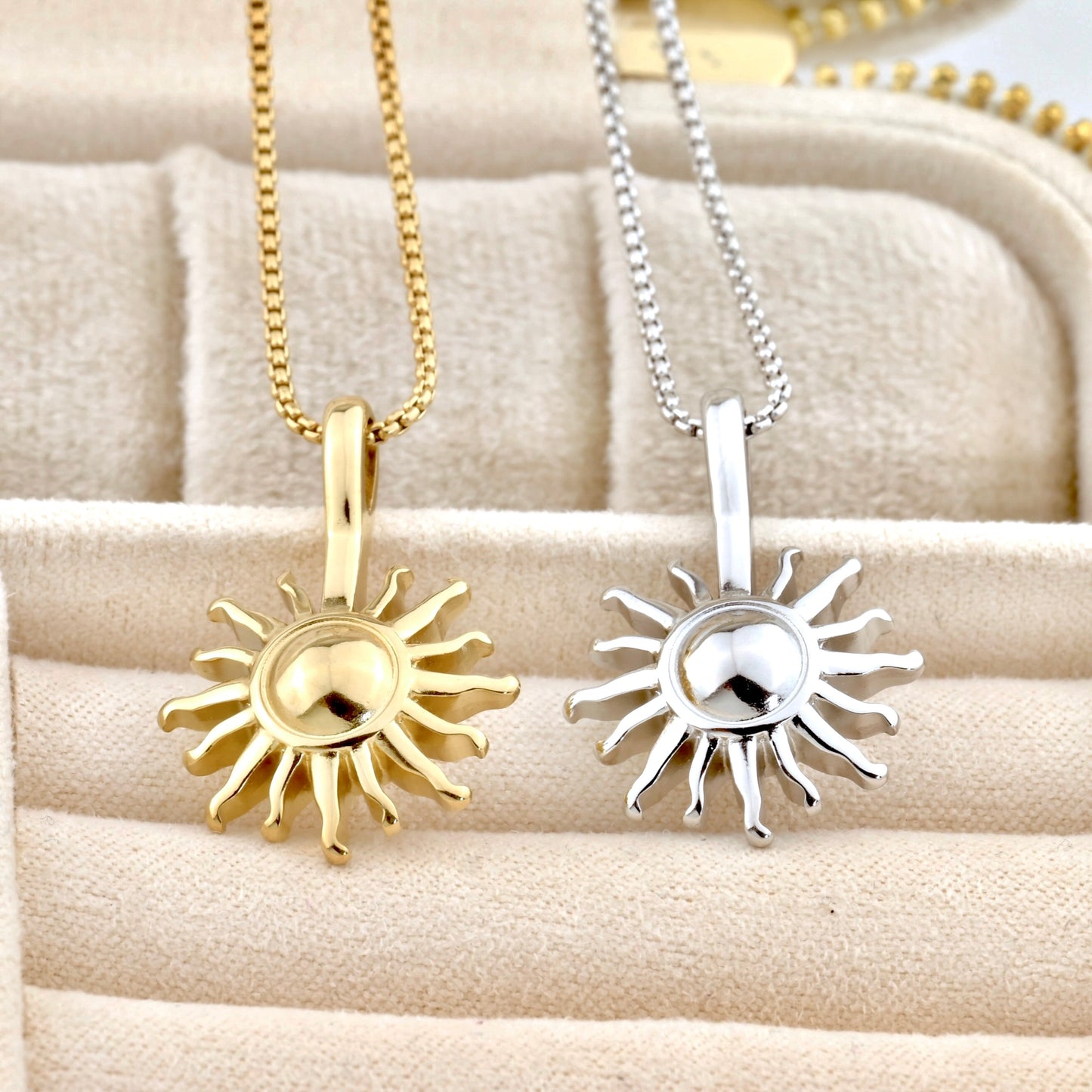 Gold and silver sun-shaped pendants on chains displayed on a textured surface.