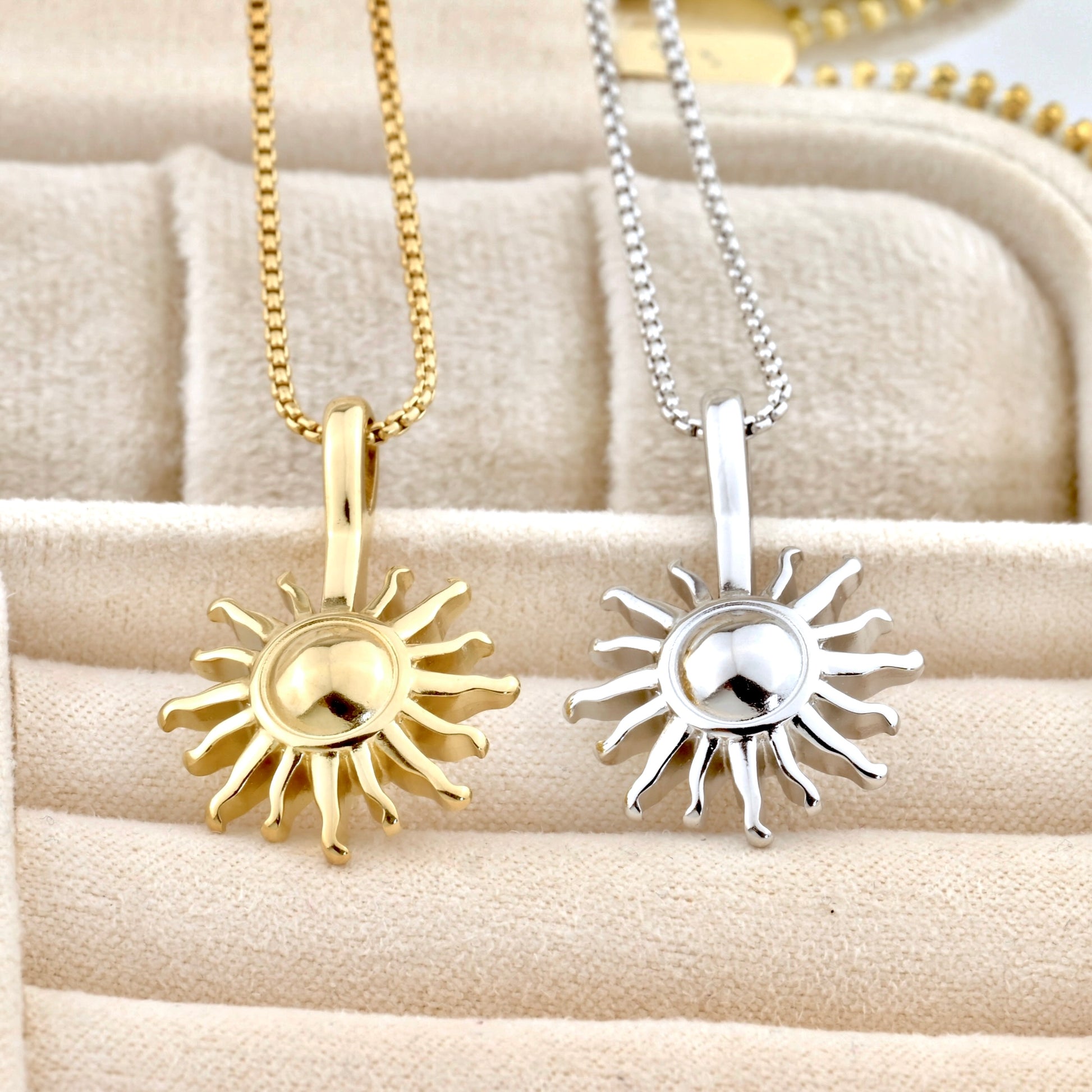 Gold and silver sun-shaped pendants on chains displayed on a textured surface.