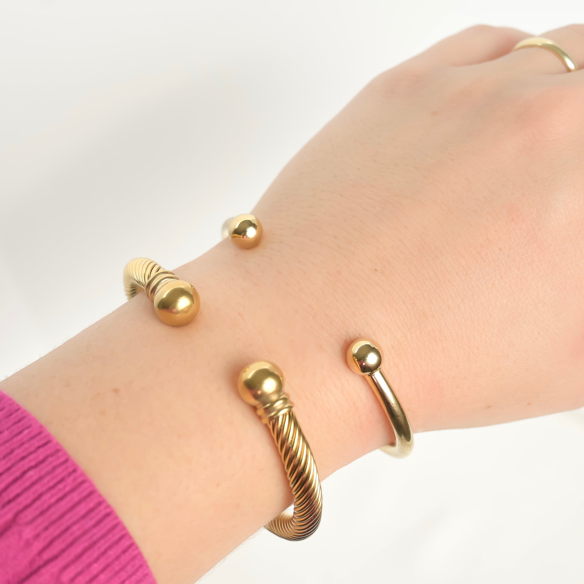 Gold plain and twisted cuff bracelets on a wrist with ball hands facing upwards