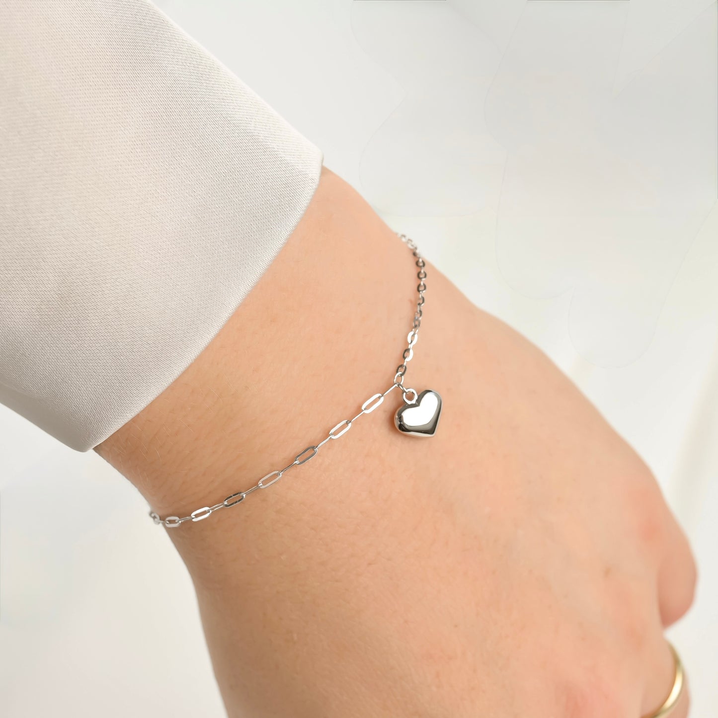 Silver heart paperclip bracelet on a person's wrist against a white background