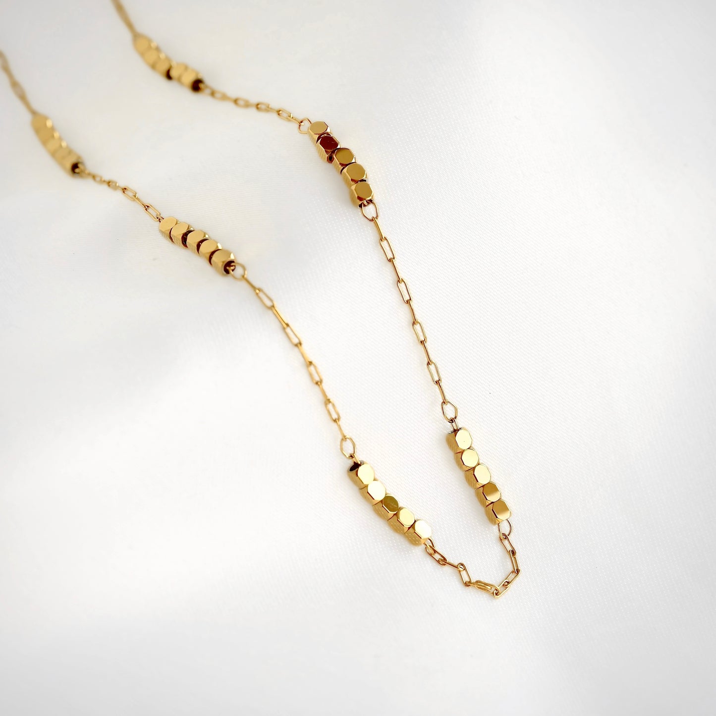 A delicate gold paperclip chain necklace featuring multiple small gold cube beads displayed on a clean white background.