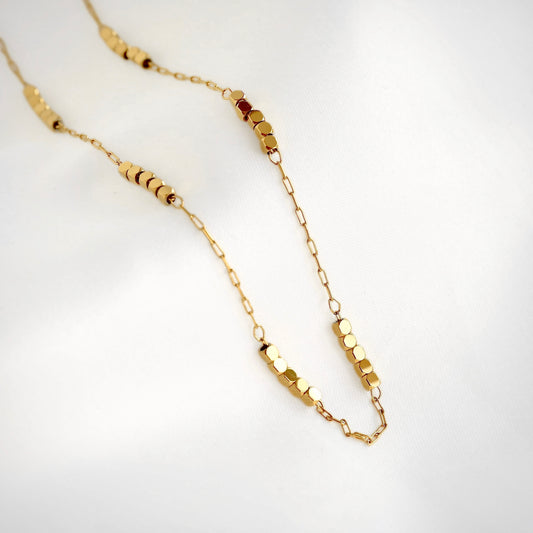 A delicate gold paperclip chain necklace featuring multiple small gold cube beads displayed on a clean white background.