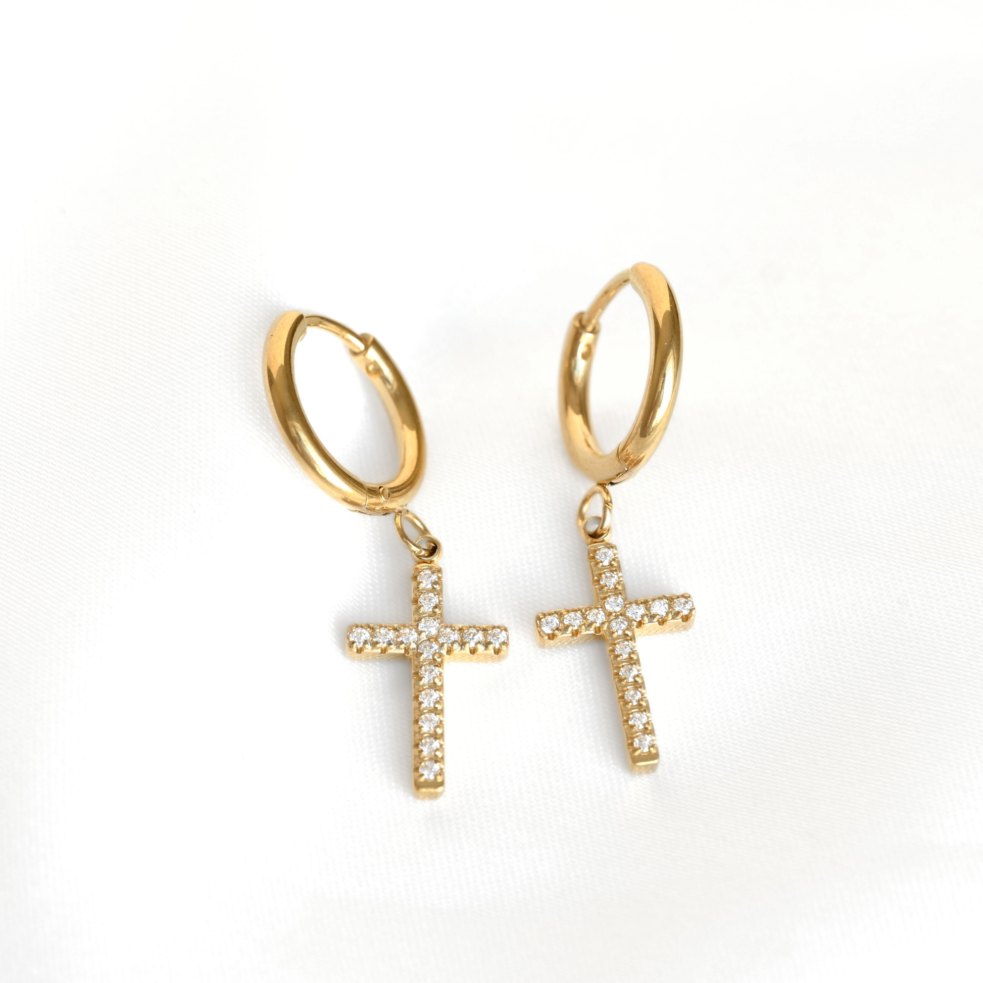 A pair of gold cross hoop earrings with dangling cross charms paved with small clear stones, shown on a plain white background.