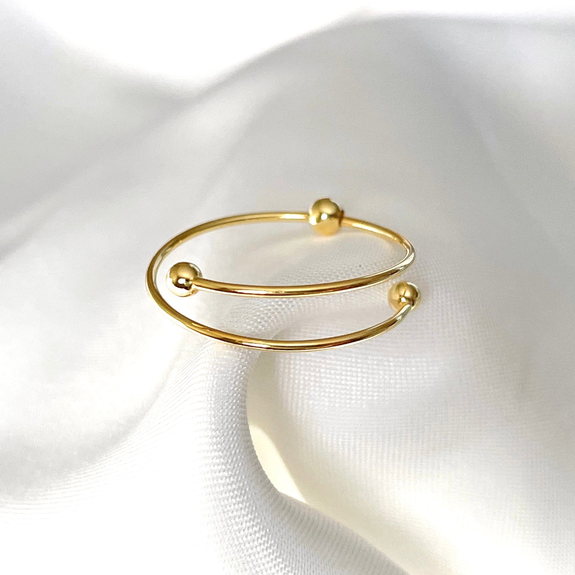 Dlicate gold wrap ring with three beads on a white fabric background