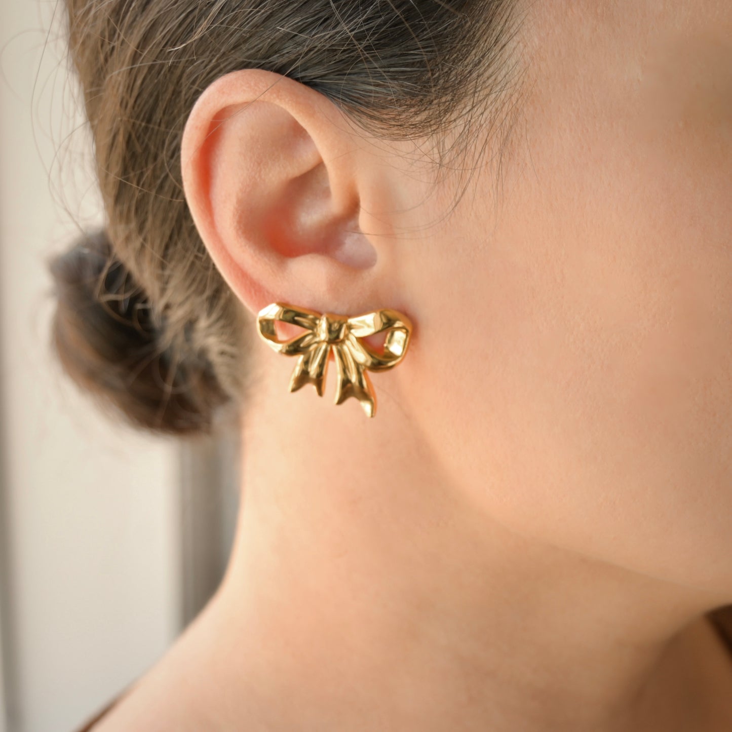 Close up of Gold bow tie earring worn by a person with a neutral background
