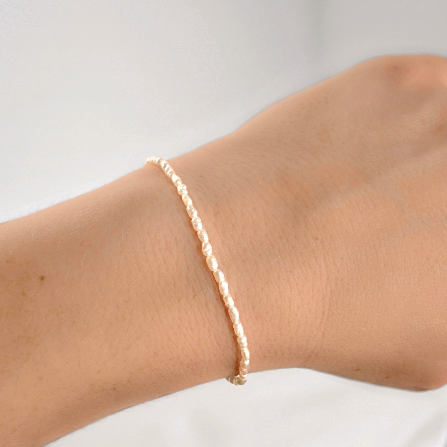 A delicate, thin gold pearl bracelet worn on a person's wrist against a plain white background.