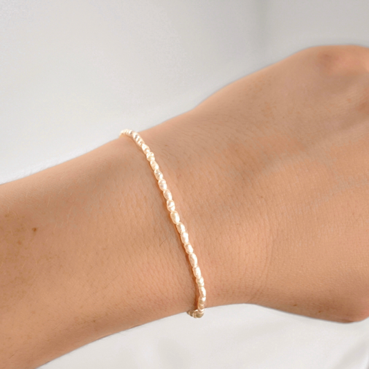 A delicate, thin gold pearl bracelet worn on a person's wrist against a plain white background.