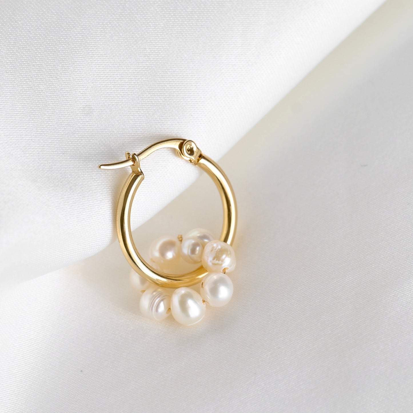 One thin gold hoop earring with natural pearls on a white background
