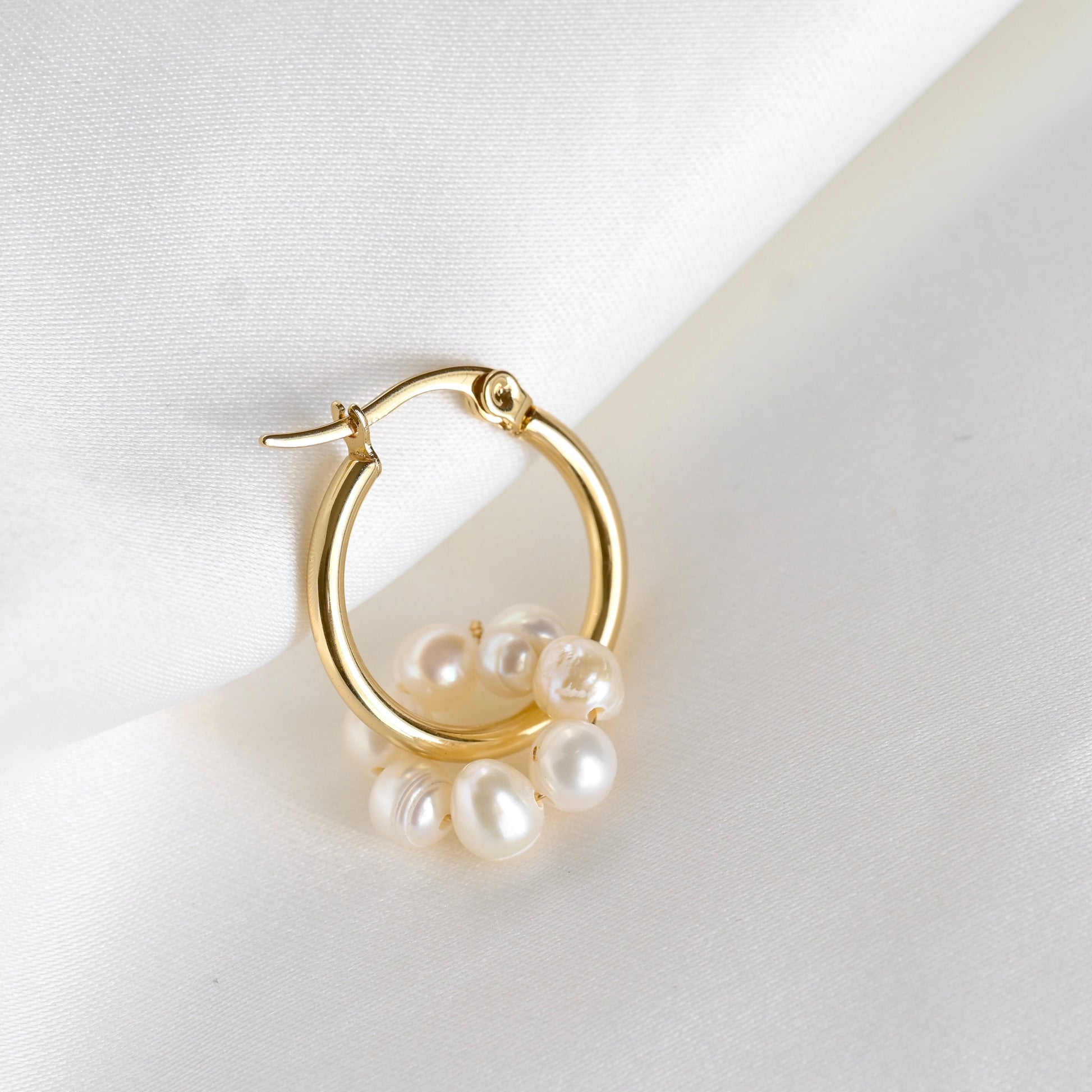One thin gold hoop earring with natural pearls on a white background
