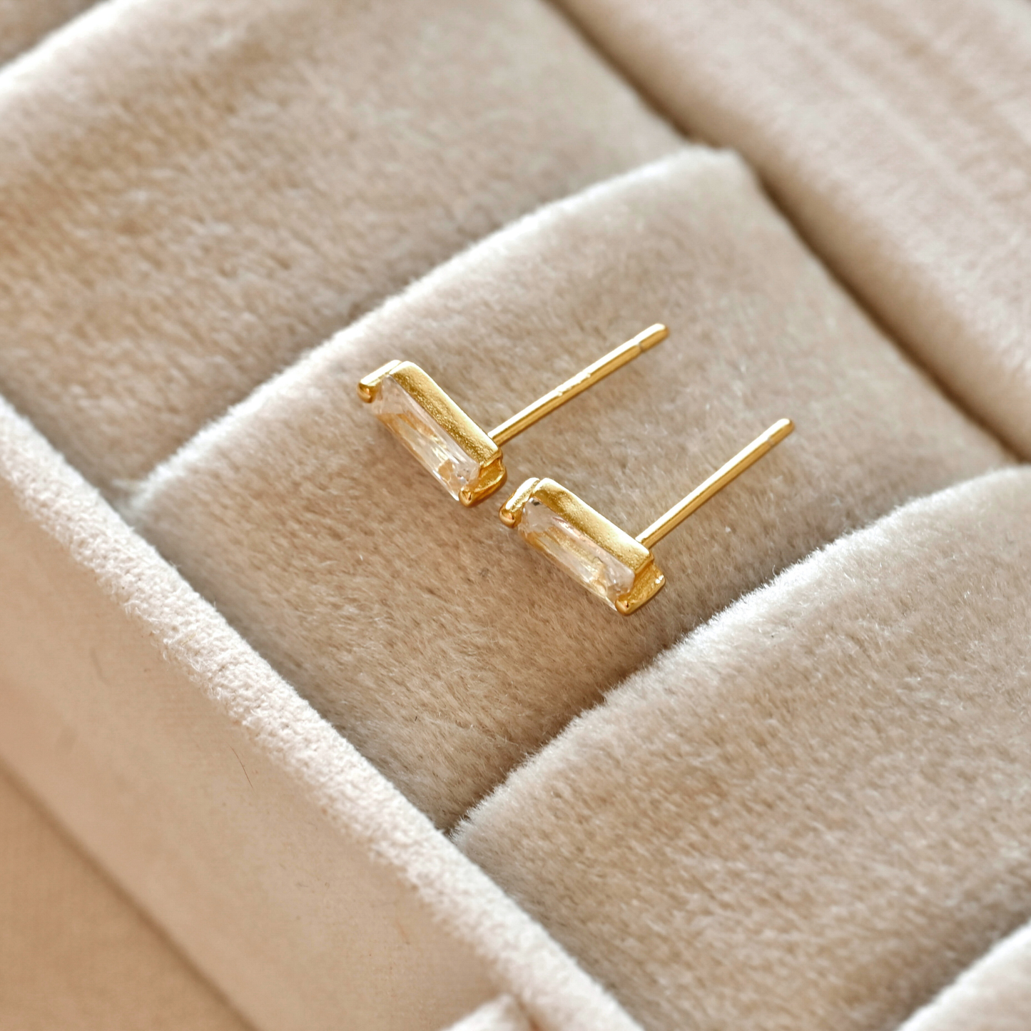 Gold  baguette stud earrings on a beige jewelry box