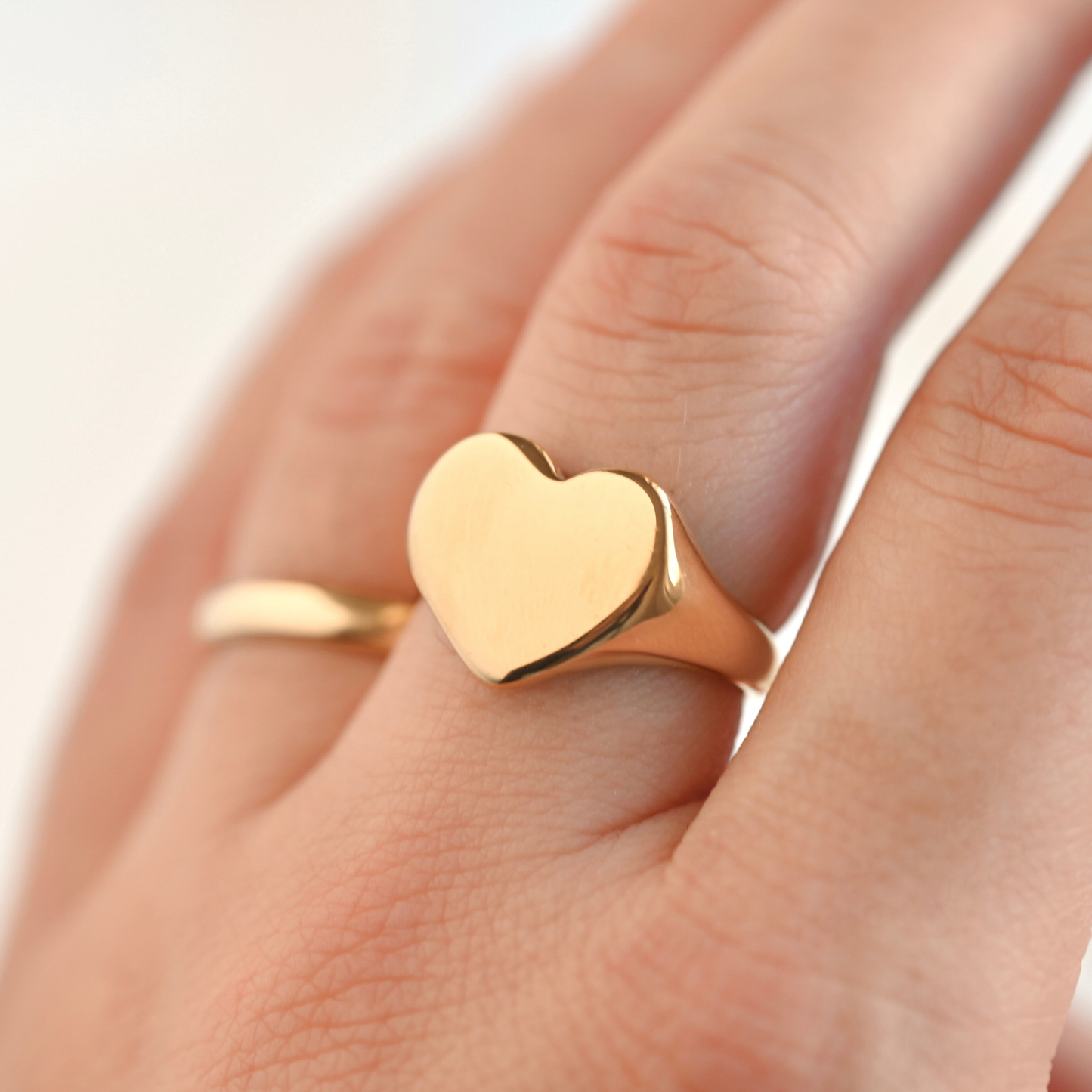Gold heart signet ring on a finger with a blurred background