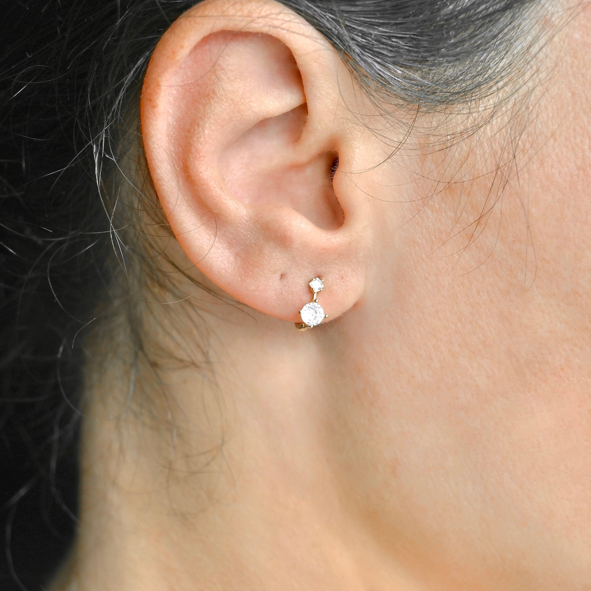 Close-up of an ear wearing a small huggie earring with a clear gemstone.