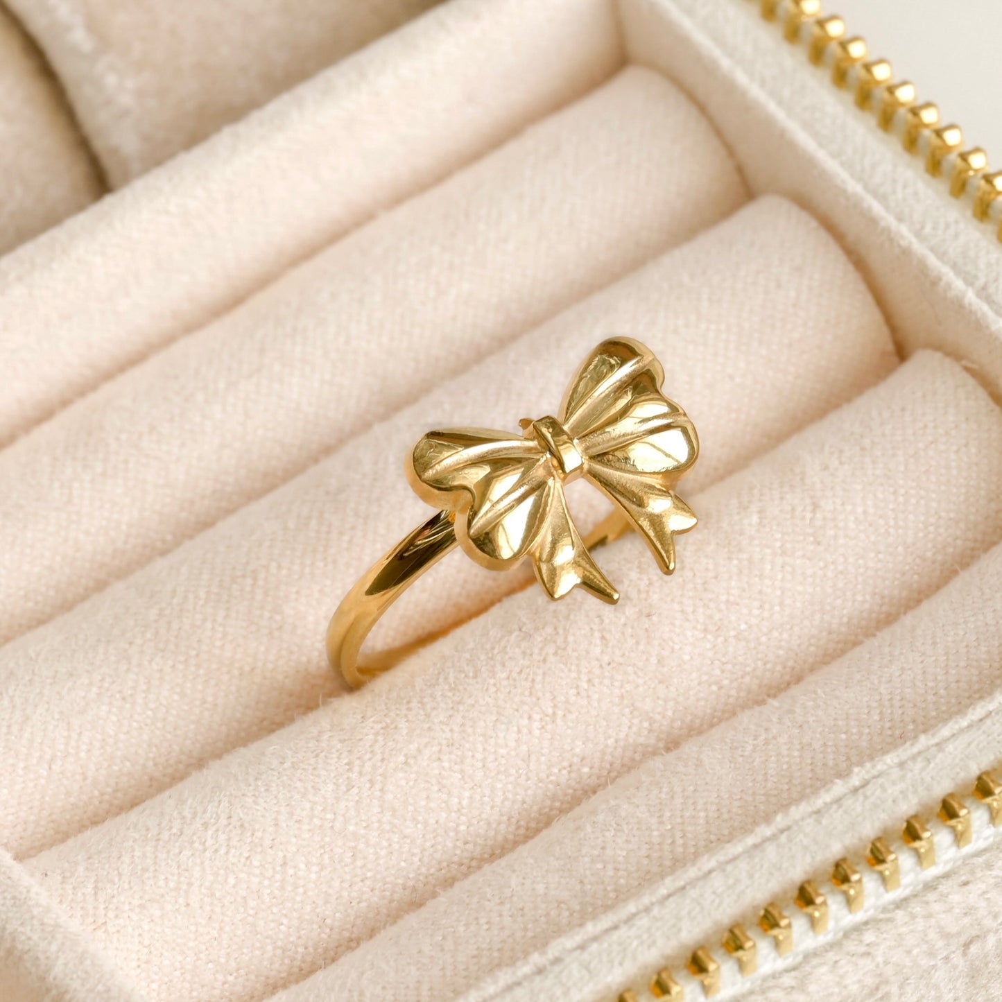 Gold bow-shaped ring in a beige ring tray