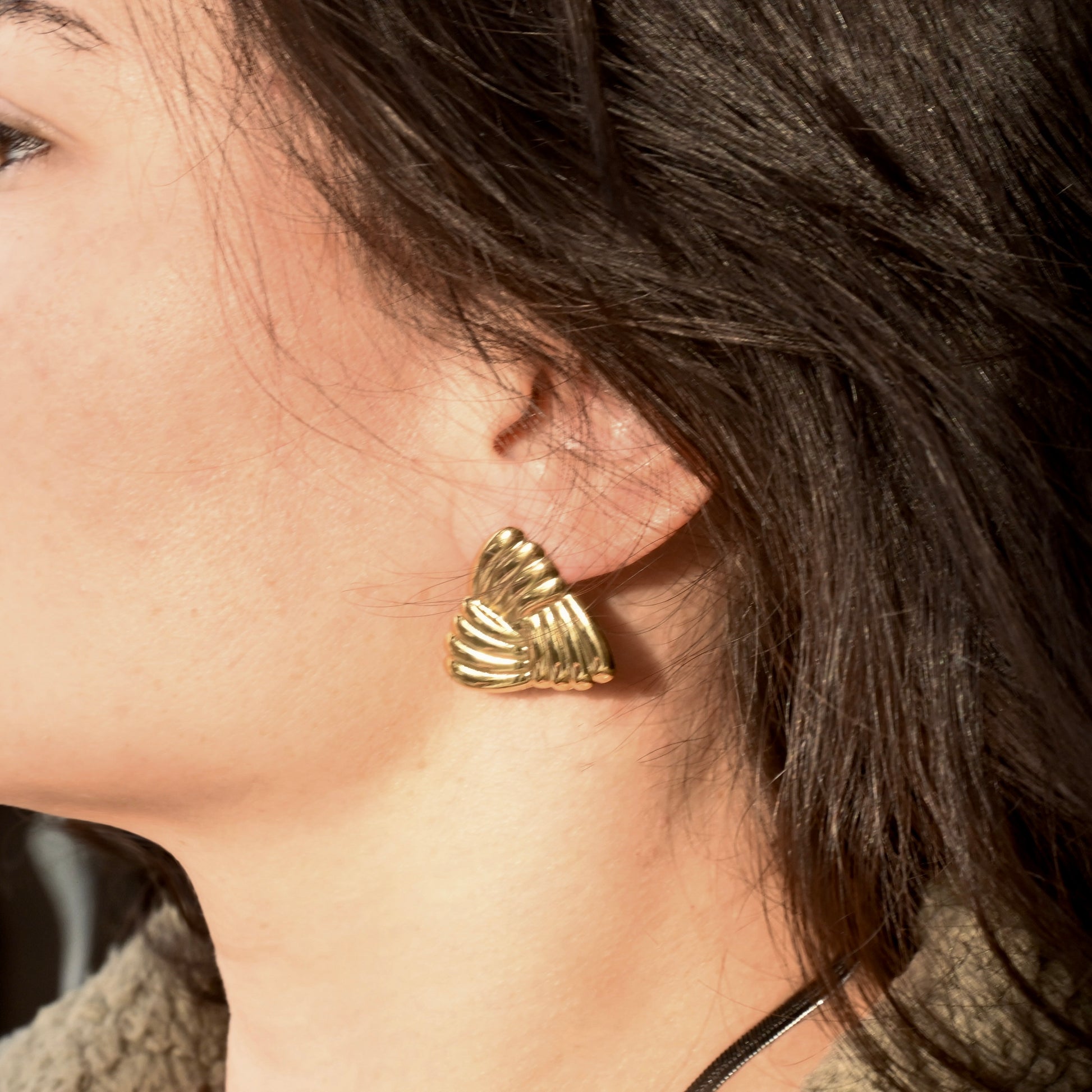 Close-up of a person wearing gold  triangle earrings with a textured design.