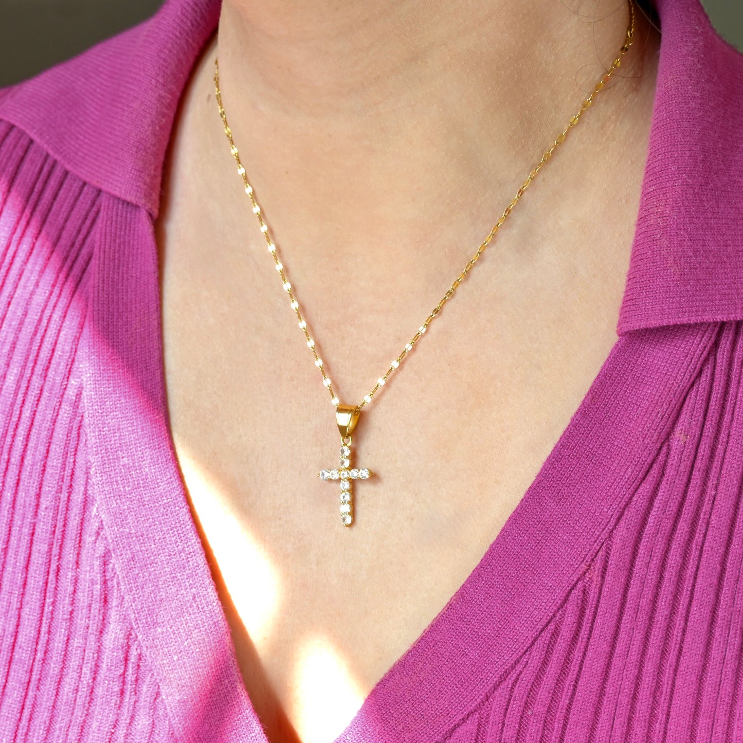 Gold CZ cross necklace on a person wearing a pink top