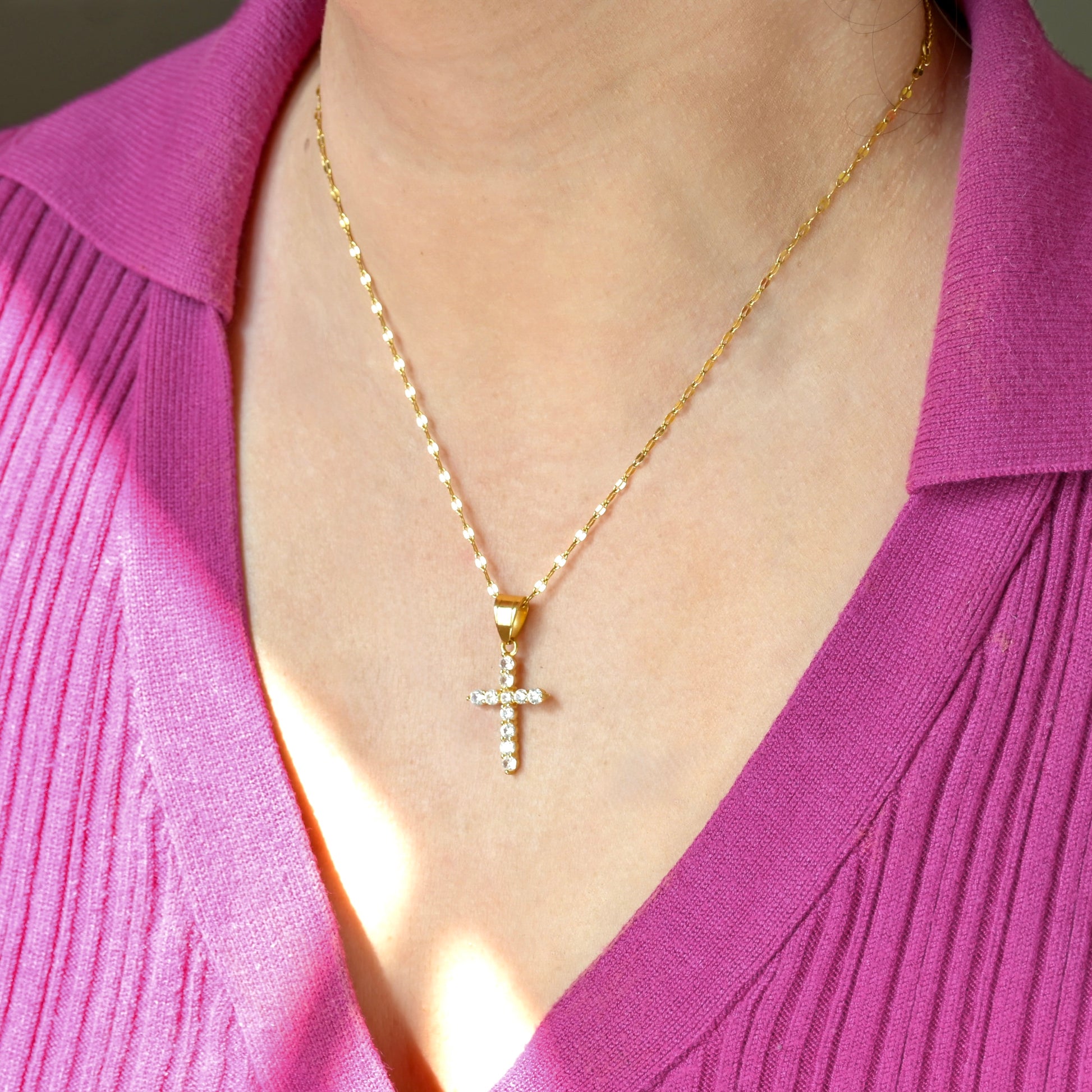 Gold CZ cross necklace on a person wearing a pink top