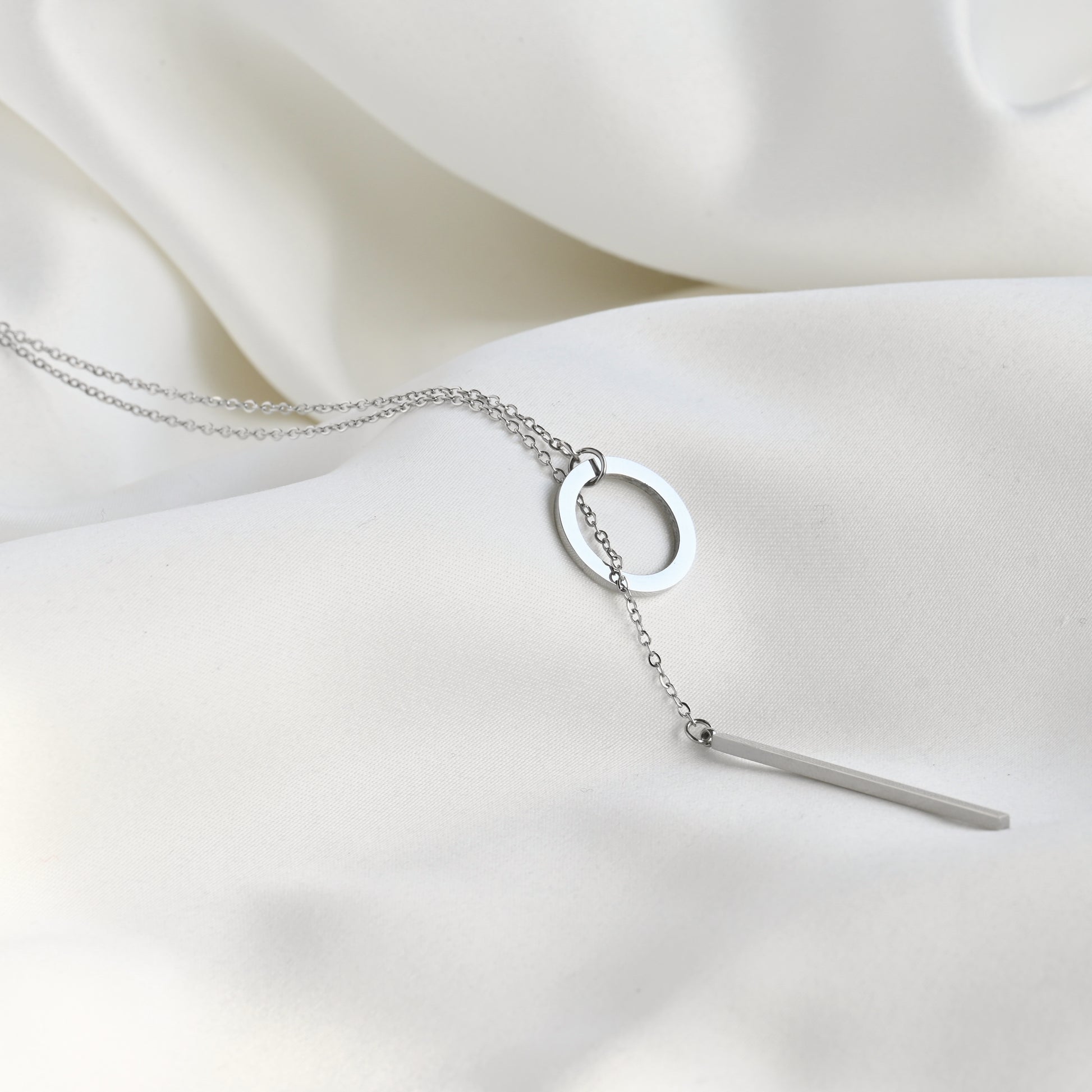 Silver  Y shaped necklace with a circle-bar pendant on a white fabric background