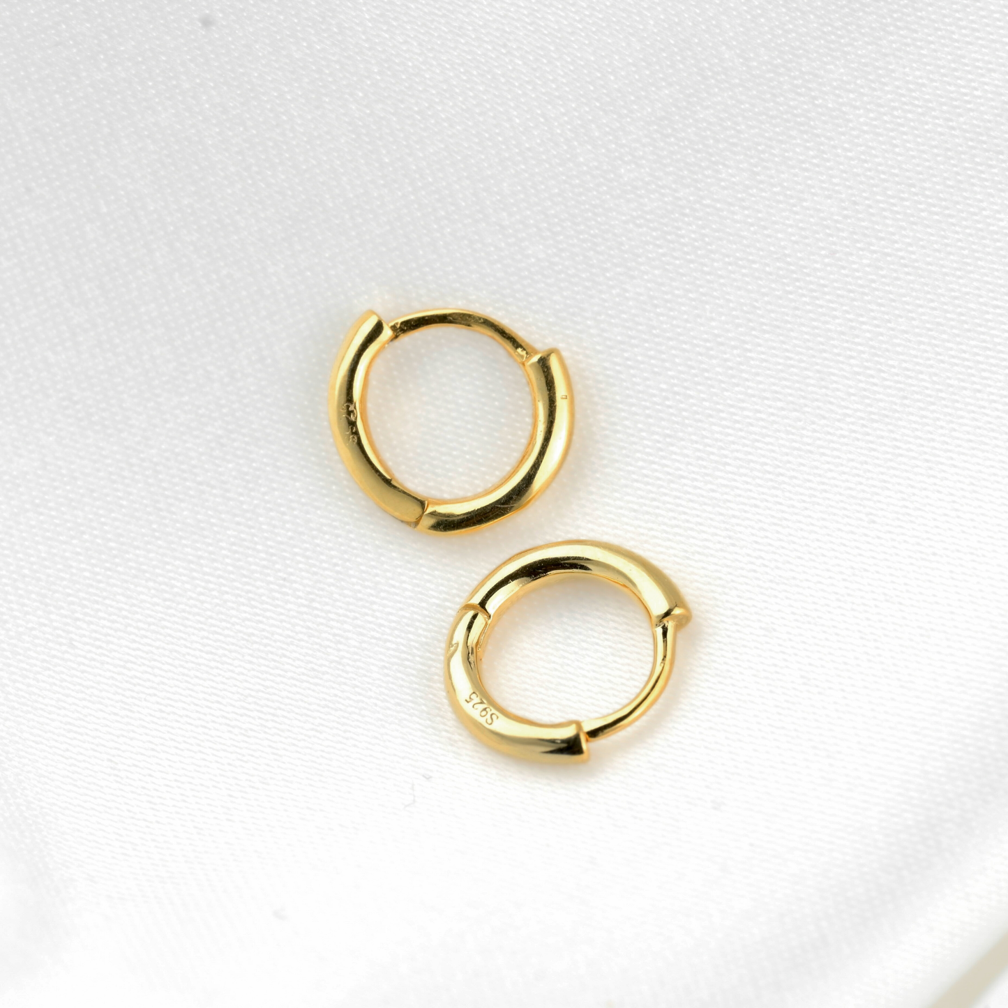 Gold slim tunnel hoop earrings on a light gray background