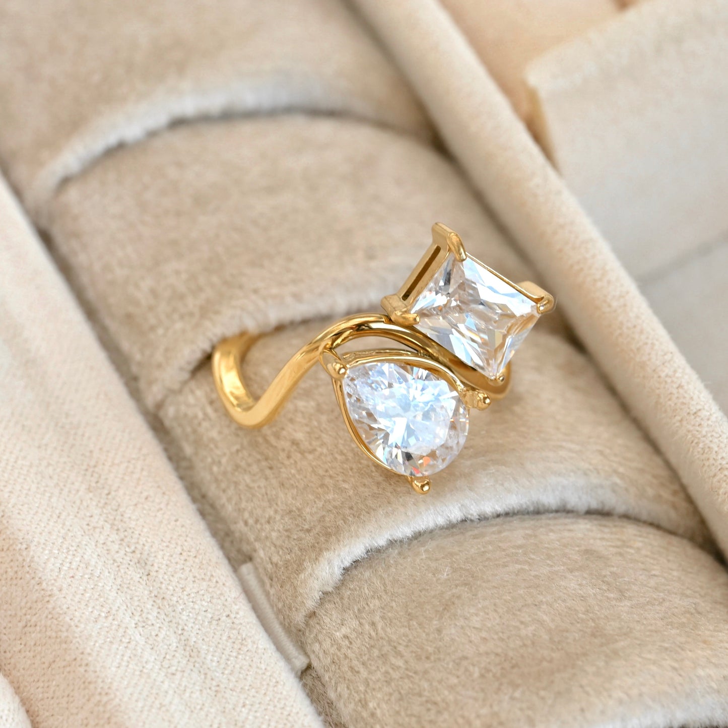 Gold ring with large pear and emerald-cut  Cubic zirconia on a beige fabric background