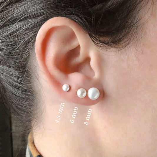 Close-up of an ear wearing three pearl stud earrings with size labels.
