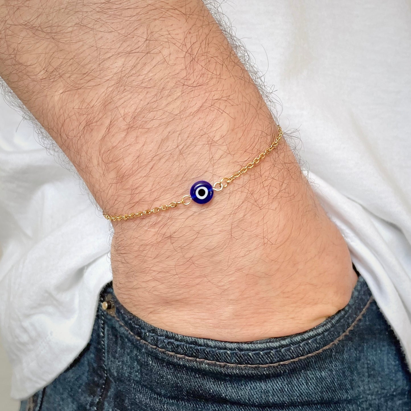 Gold evil eye bracelet with a blue evil eye charm on a man's wrist.