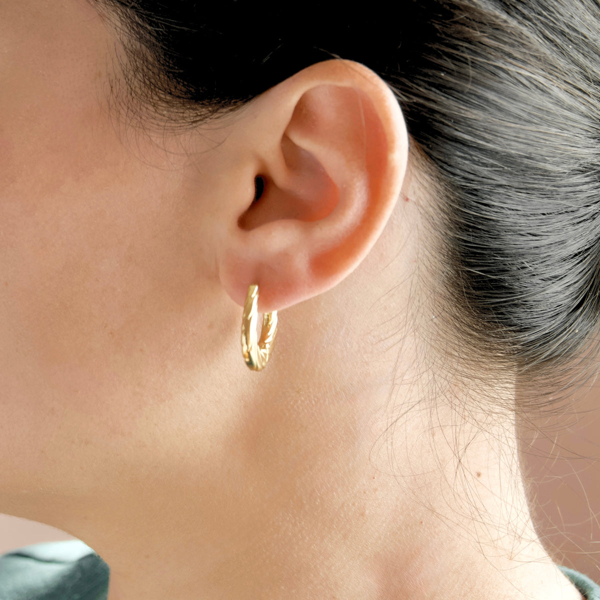 A close-up of a person's ear wearing a small gold huggie hoop earring.