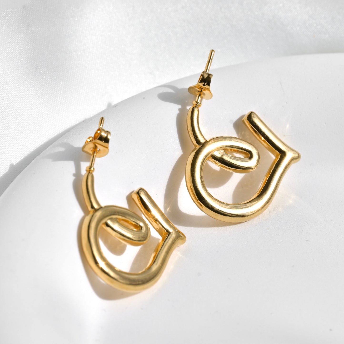 Gold heart hoop earrings on a white background under direct sunlight