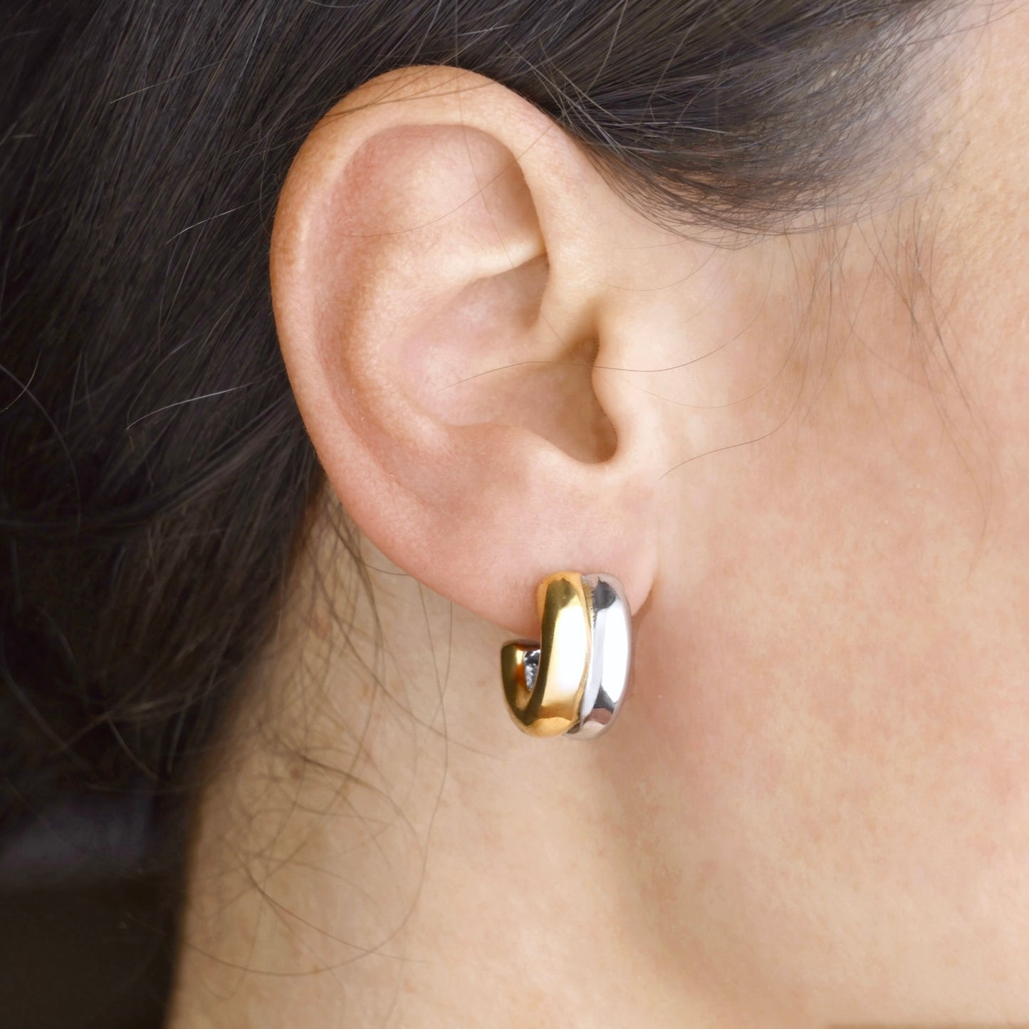Mixed metal hoop earring worn on an ear with dark hair.