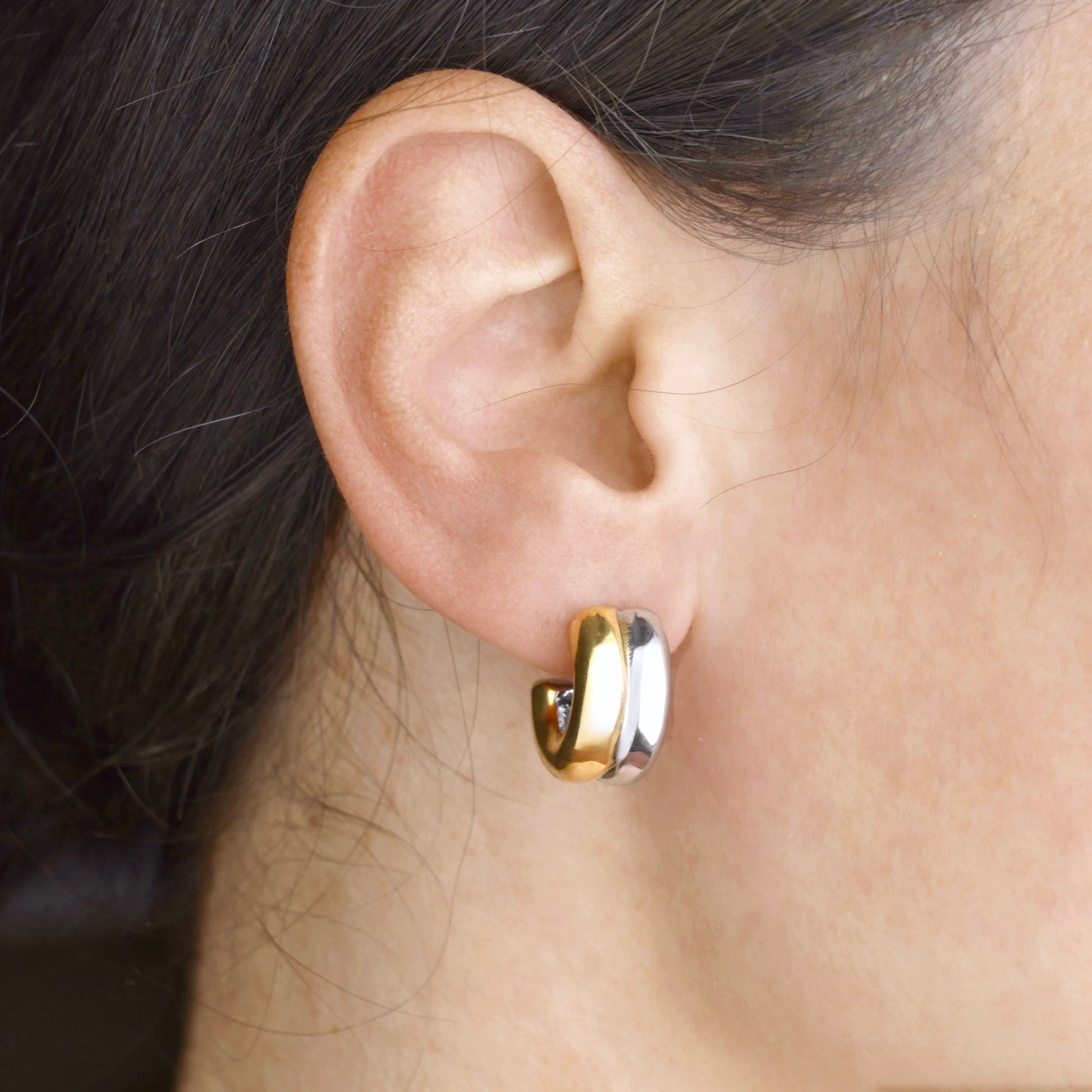 Mixed metal hoop earring worn on an ear with dark hair.