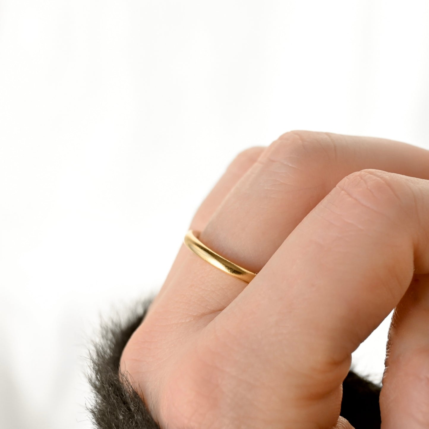 Side profile view of a thin band on a women's finger against white background