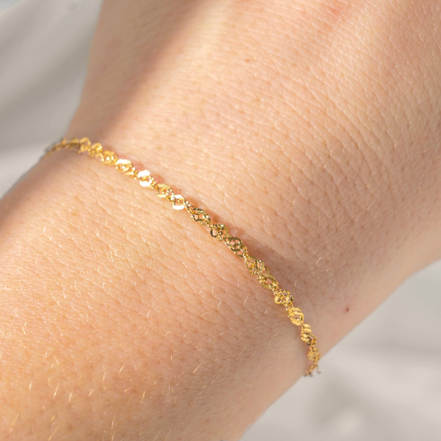 Gold sparkling chain bracelet on a wrist with a neutral background