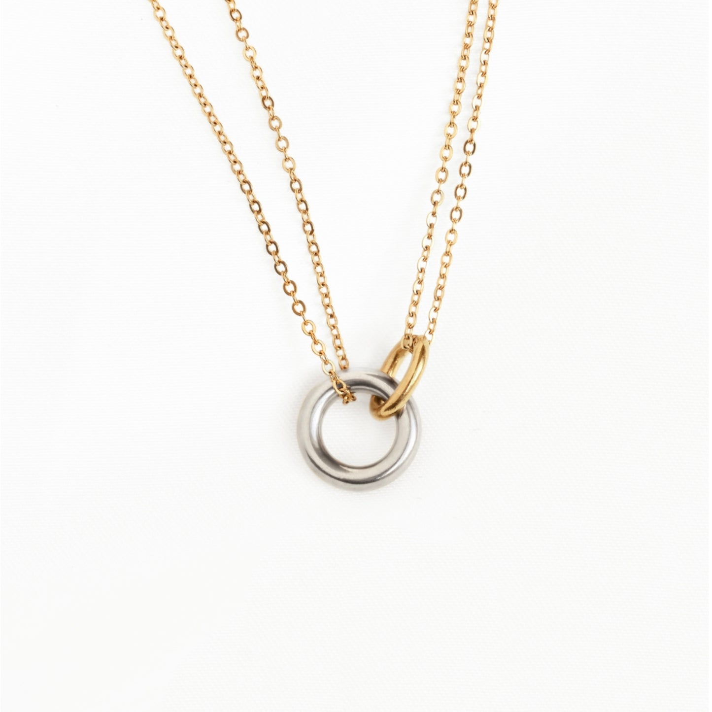 A delicate two-tone necklace featuring a fine gold cable chain, a small gold ring connector, and a double-ring pendant with one polished gold ring and one silver-toned ring, set against a plain white background.